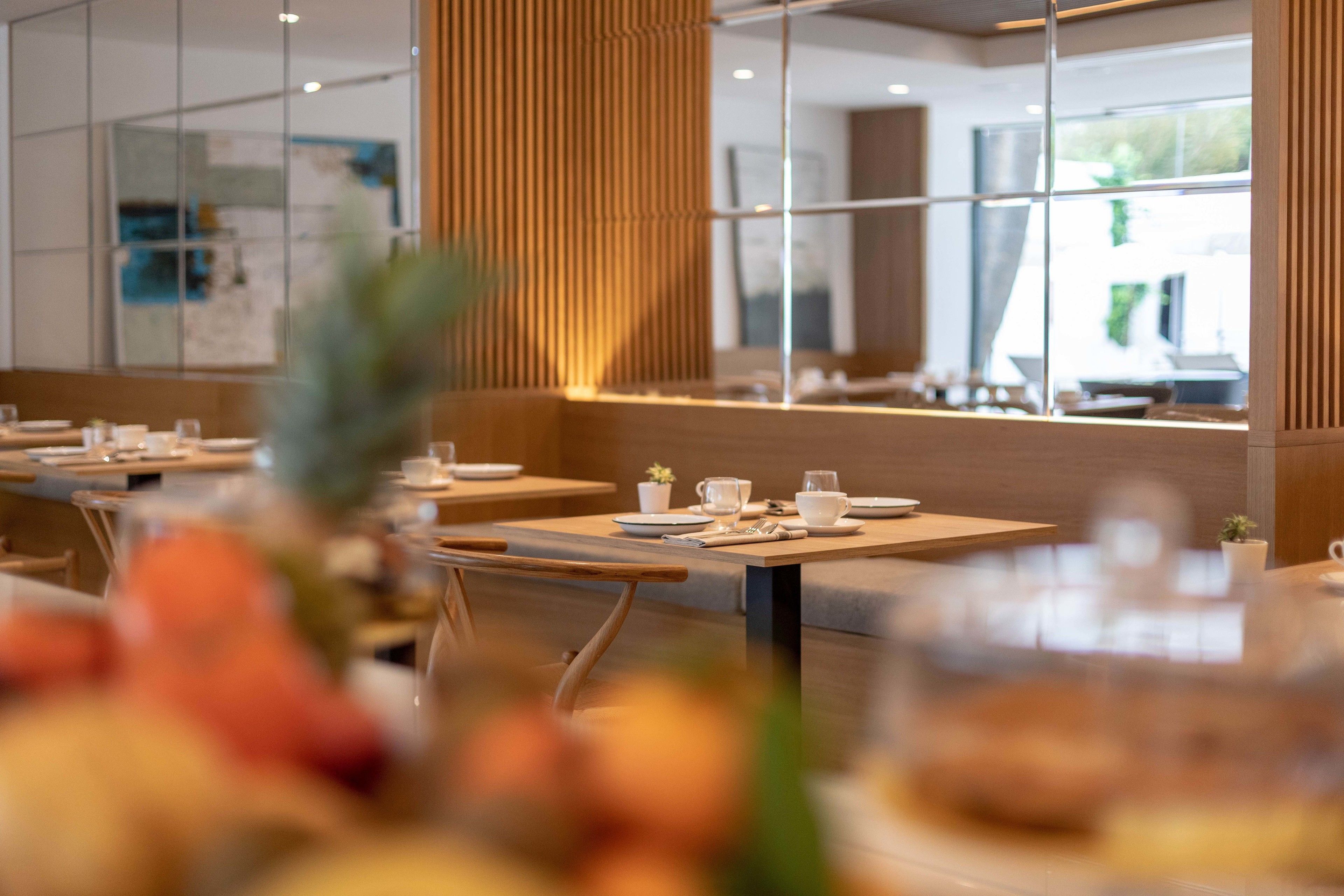 Un interior de restaurante moderno con paneles de madera, divisiones de vidrio y mesas ordenadas con vajilla blanca.
