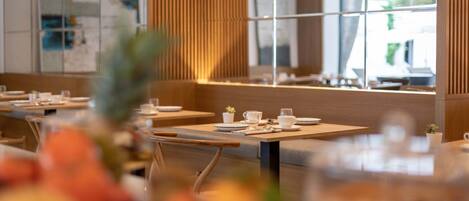 A modern restaurant interior with wooden paneling, glass partitions, and neatly arranged tables with white tableware.