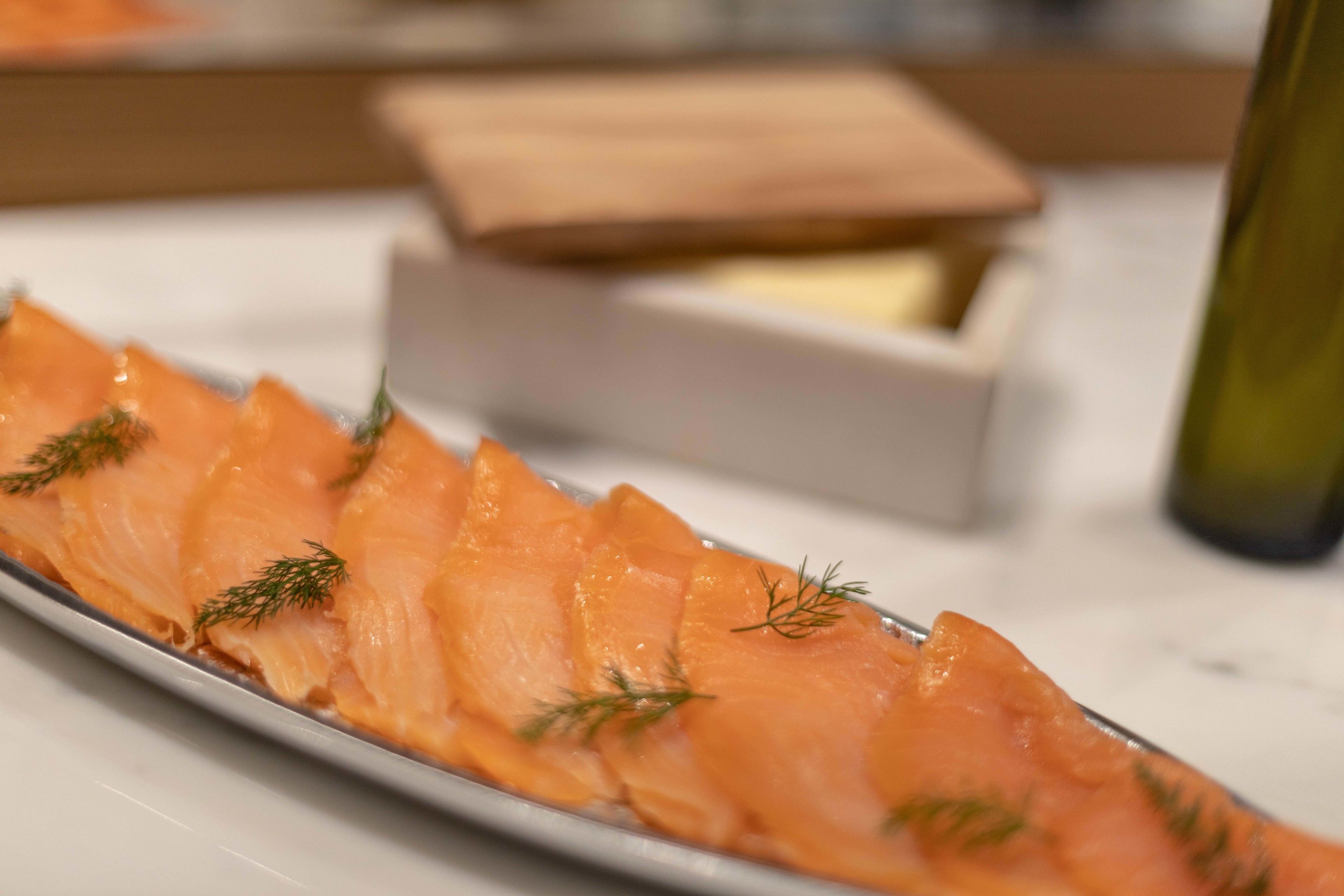 A plate of smoked salmon garnished with dill, with a wooden box and a bottle in the background.