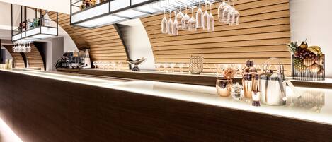 Un'area bar moderna con parete in legno, bicchieri da vino, bottiglie e attrezzi da bar.
