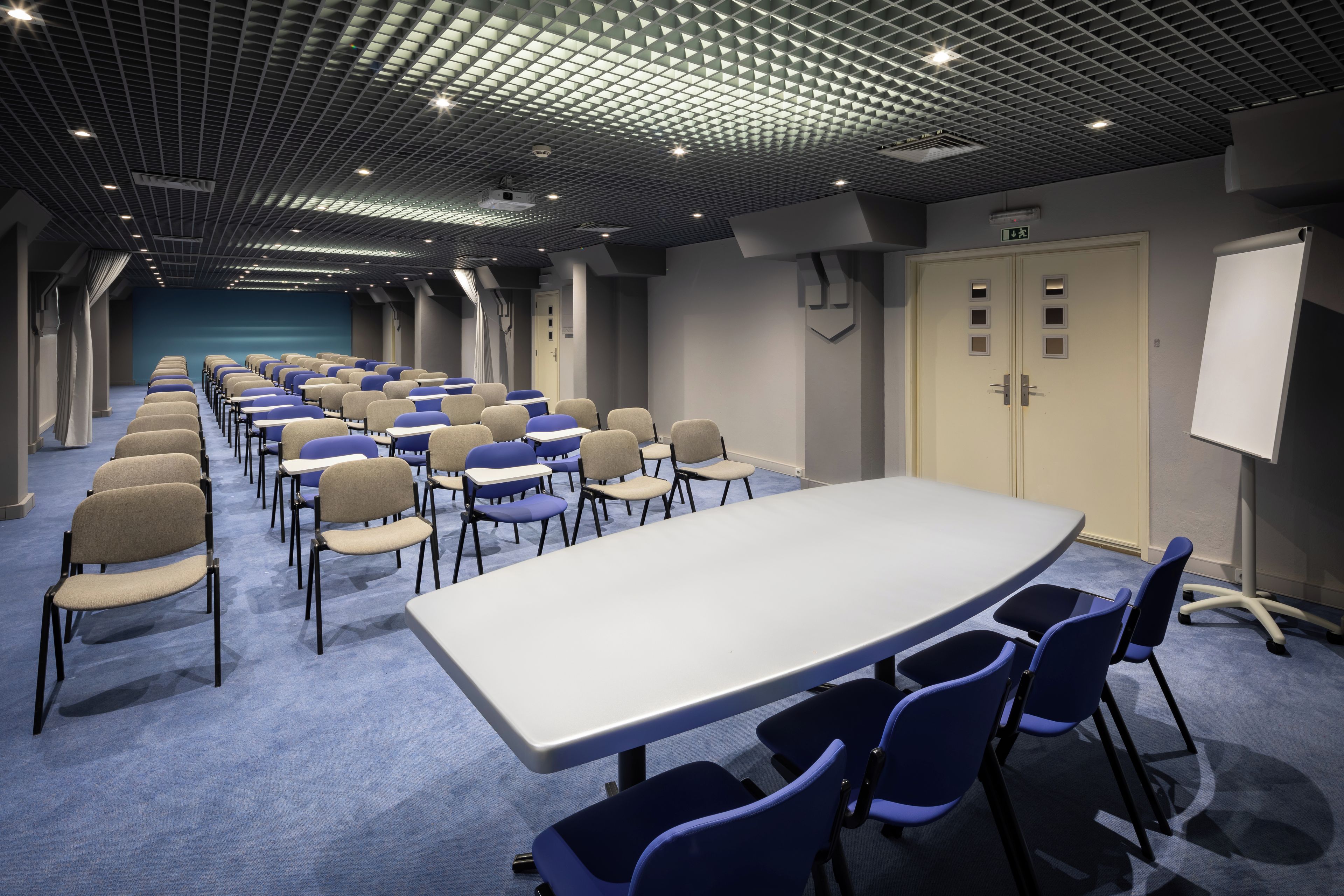 A conference room with a long table and chairs, a whiteboard, and a door with a sign.