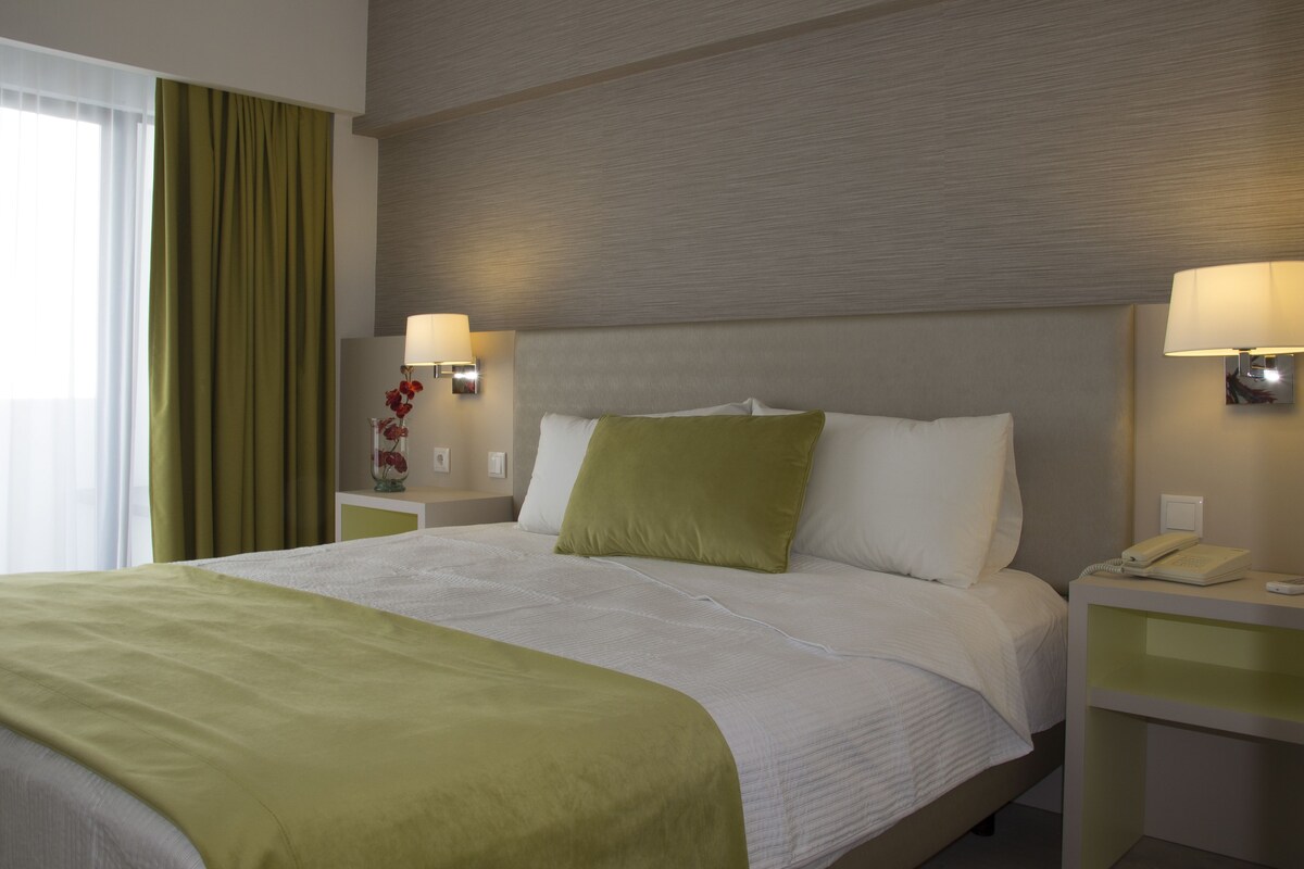 A hotel room with a large bed, green bedding, two bedside lamps, and a nightstand with a phone.