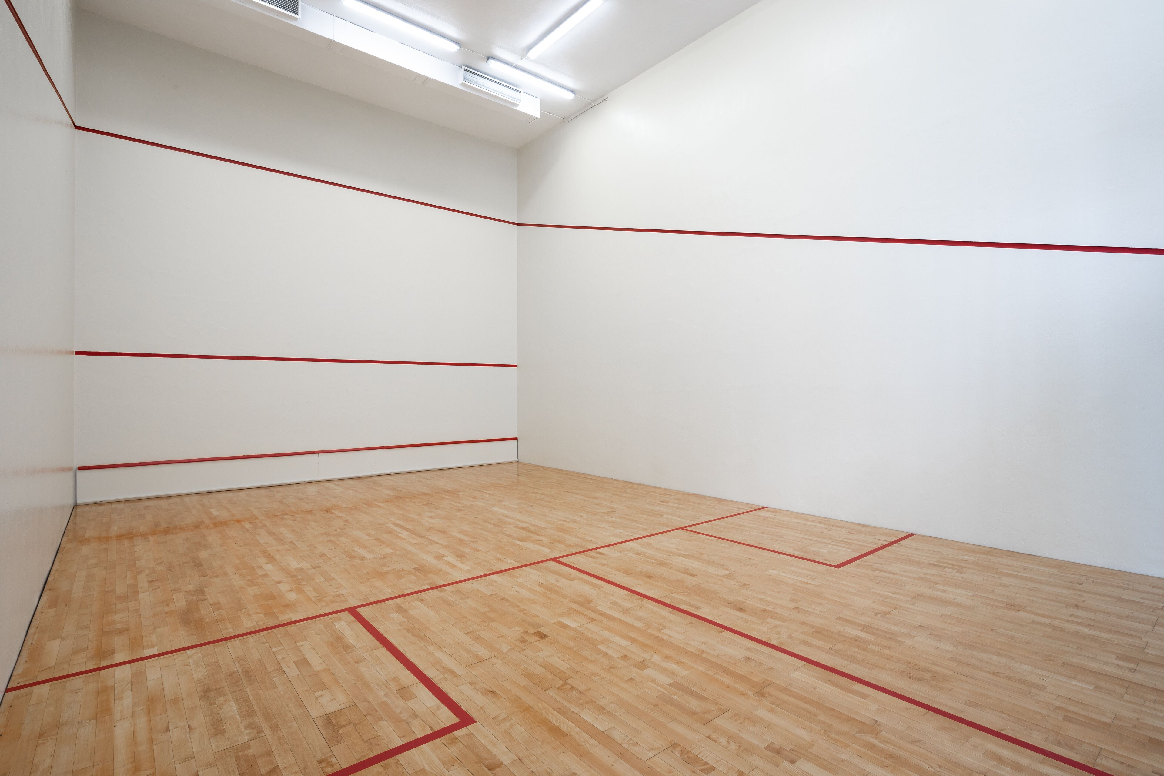 Una cancha de squash con piso de madera y líneas divisorias rojas.