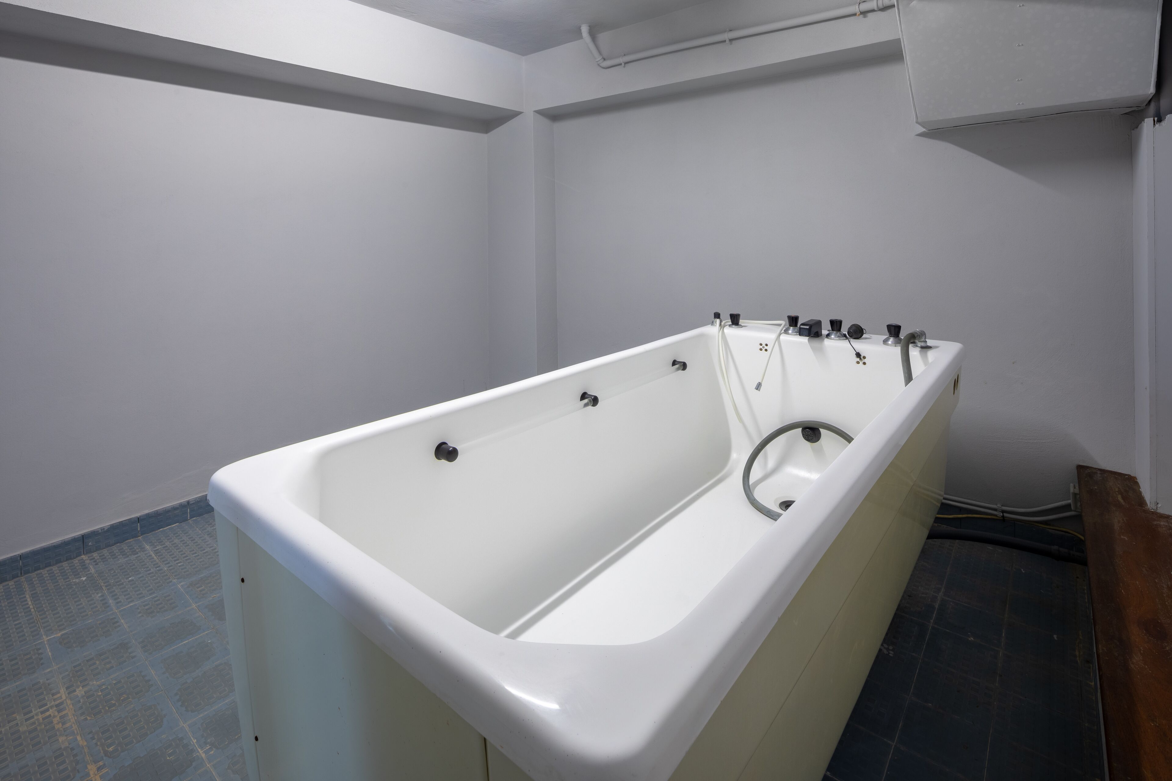Une baignoire blanche dans une salle de bain carrelée, avec un banc en bois.