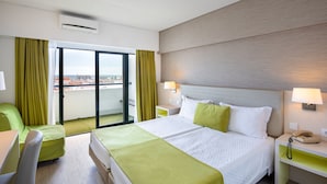 Hotellihuone, jossa on suuri sänky, työpöytä, tuoli ja lasiovesta avautuva näkymä kaupunkiin.