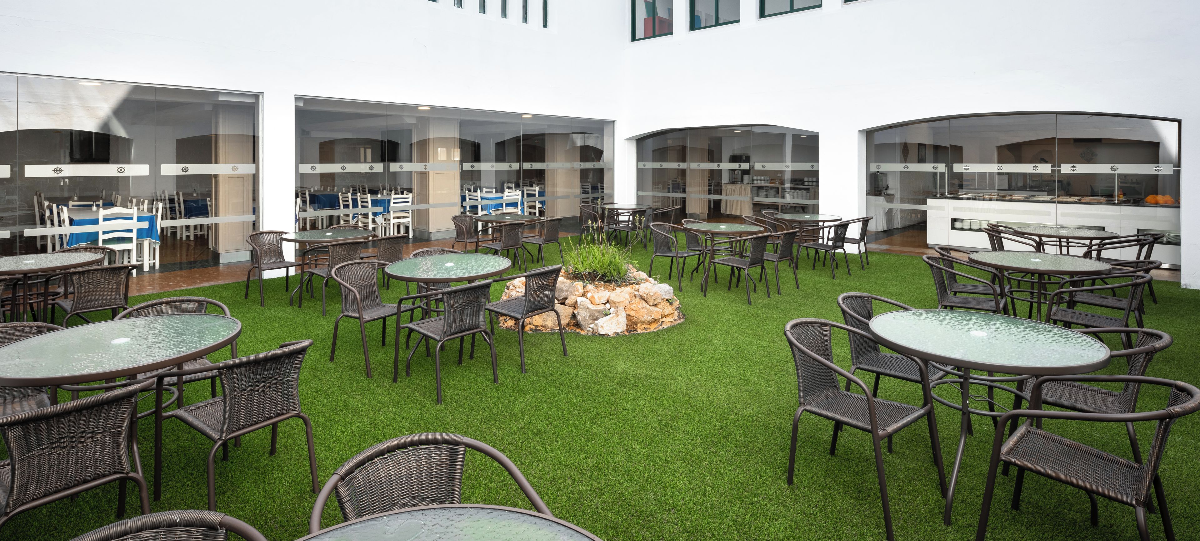 A courtyard with round tables and chairs, a central rock feature, and a glass wall.