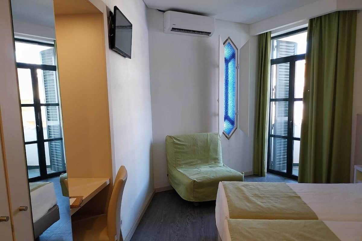 A hotel room with a bed, a chair, a desk, a TV, and a window with curtains.