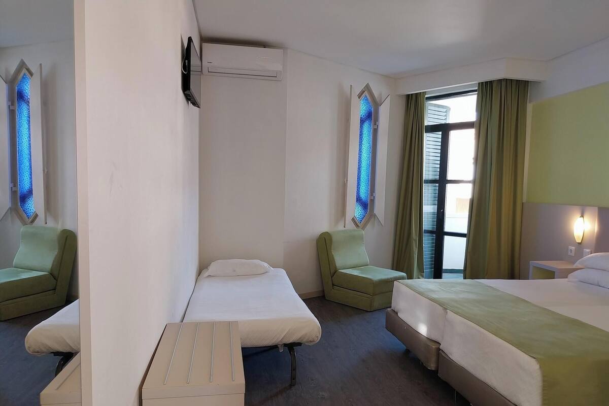 A hotel room with two single beds, a sofa, a small table, and a window with curtains.