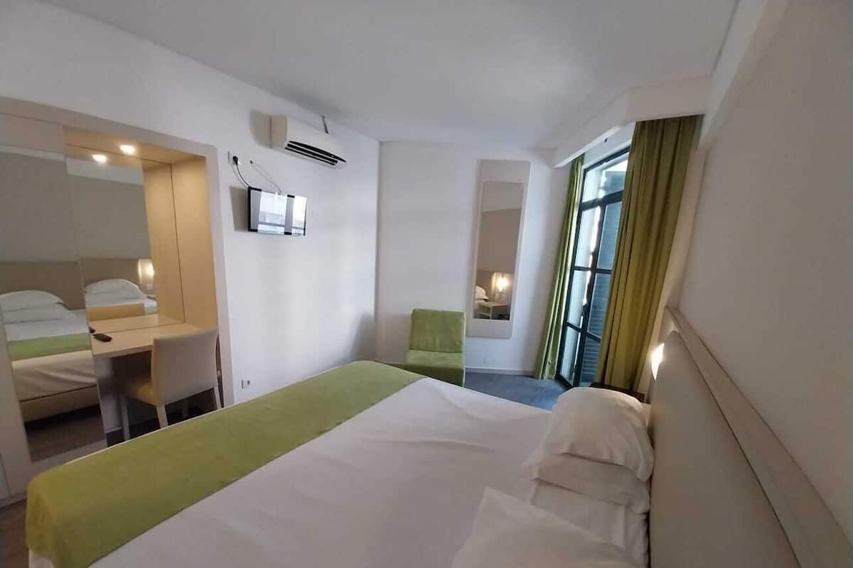 A hotel room with a large bed, a desk, a chair, and a window with curtains.