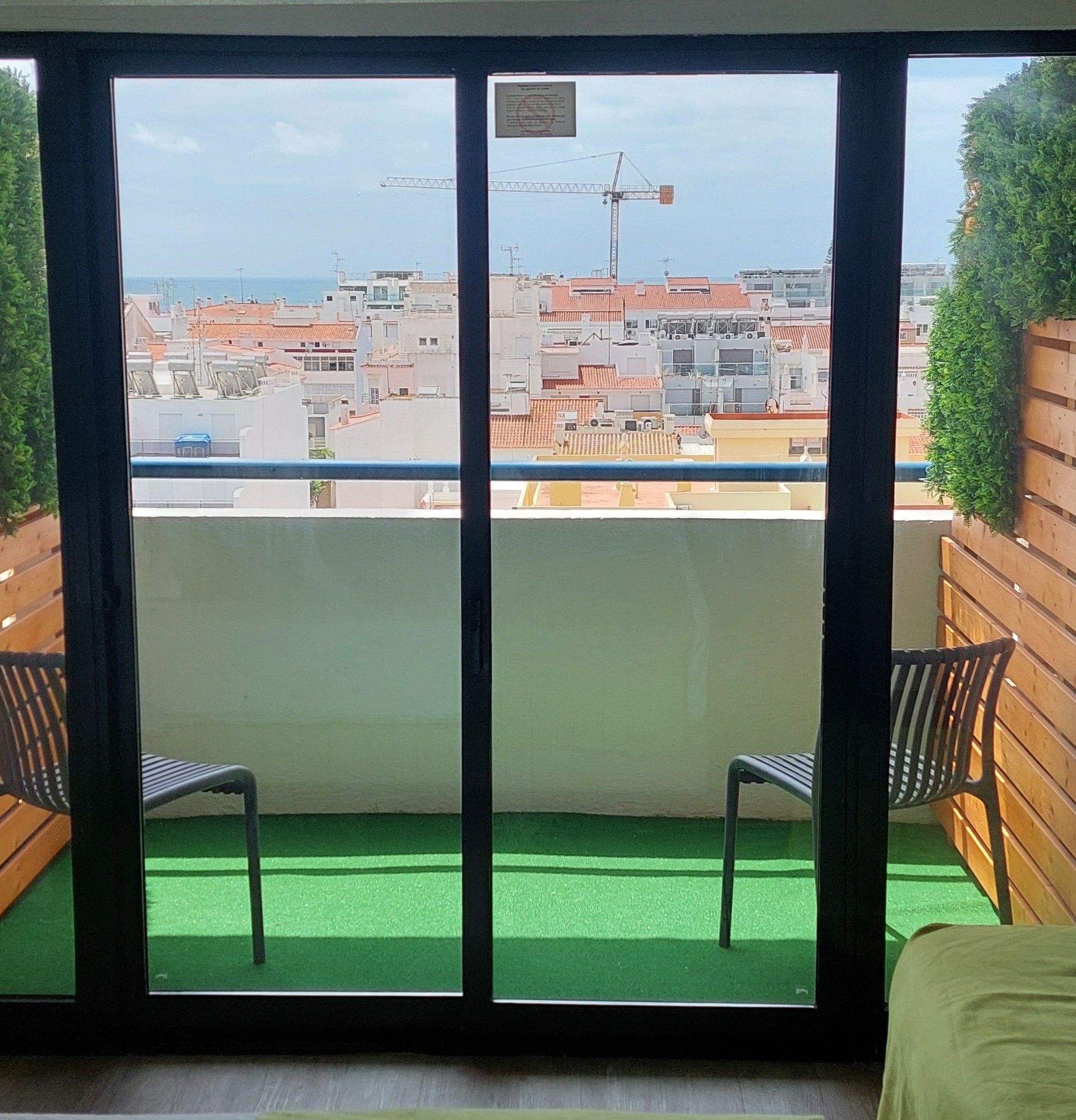 Un balcón con dos sillas, vista a un paisaje urbano y una grúa de construcción a lo lejos.