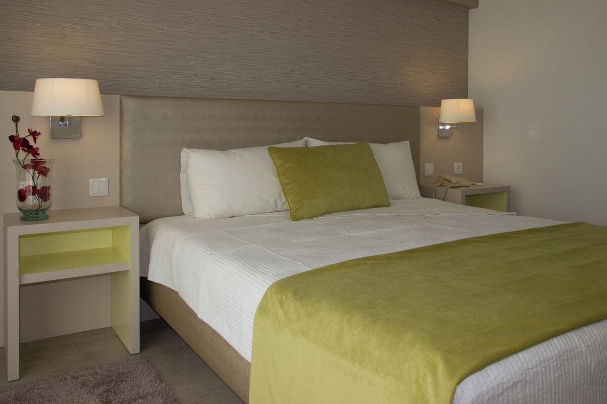 A hotel room with a large bed, two bedside tables, a nightstand, a lamp, and a vase with flowers.