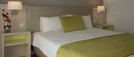 A hotel room with a large bed, two bedside tables, a nightstand, a lamp, and a vase with flowers.