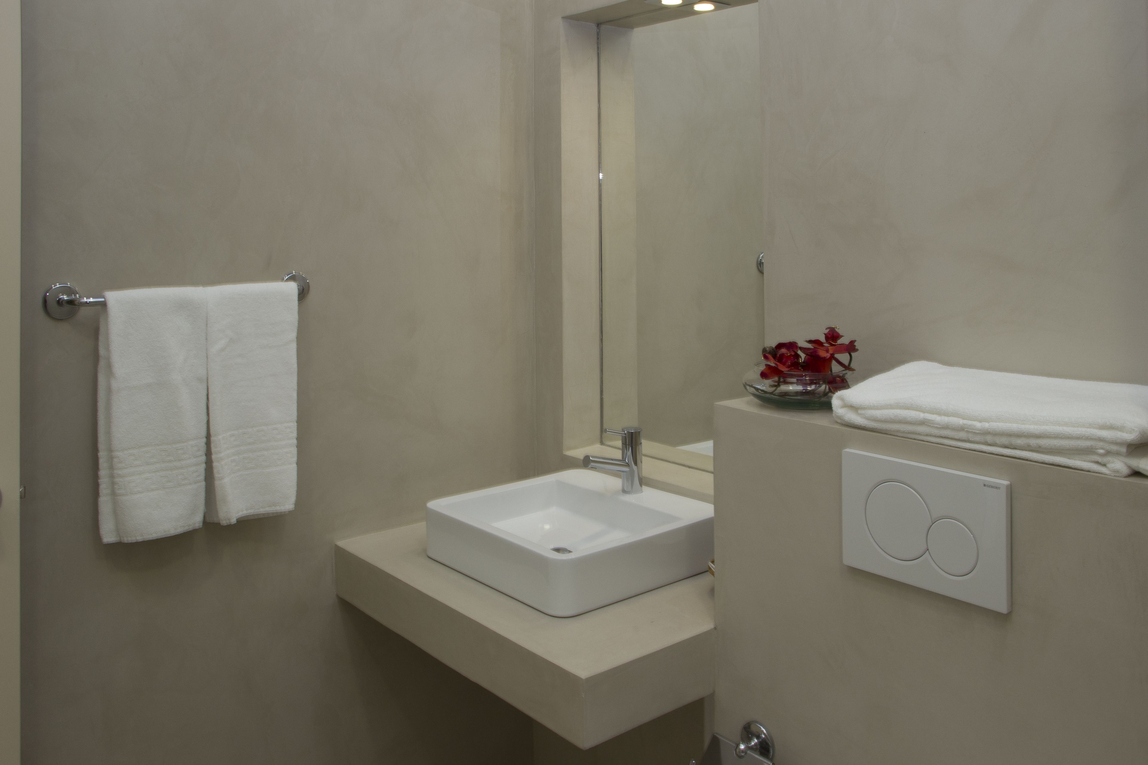 A bathroom with a white sink, a towel rack, a mirror, and a wall-mounted light switch.