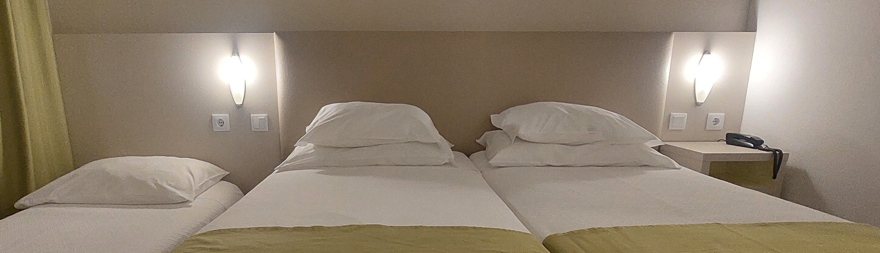 Habitación de hotel con dos camas, lámparas de noche, mesita de noche y un cortinaje.