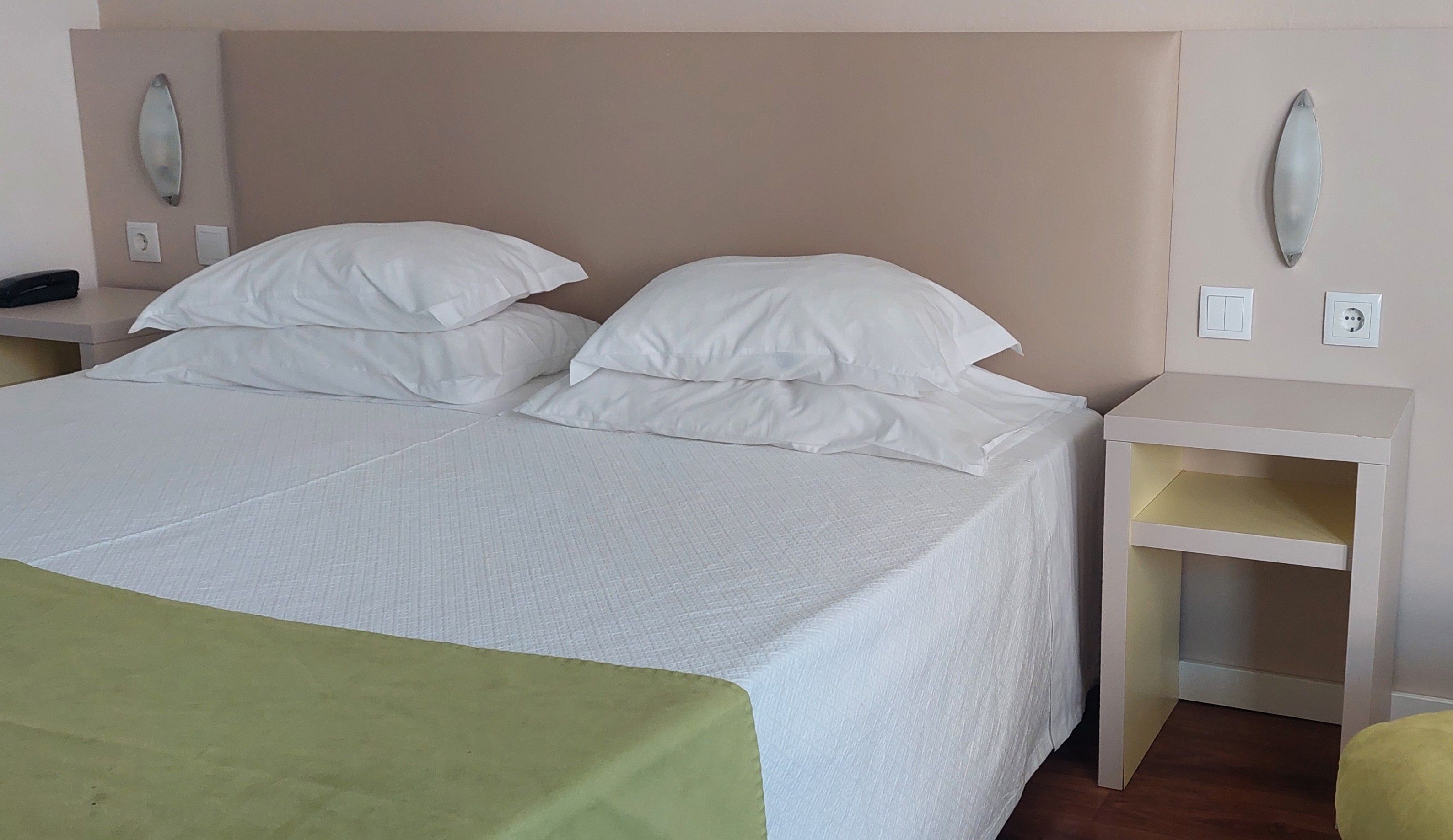 Een bed met wit beddengoed, twee nachtkastjes en een groene plaid.