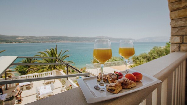 Een balkon met een ontbijttafel, met uitzicht op de kust.