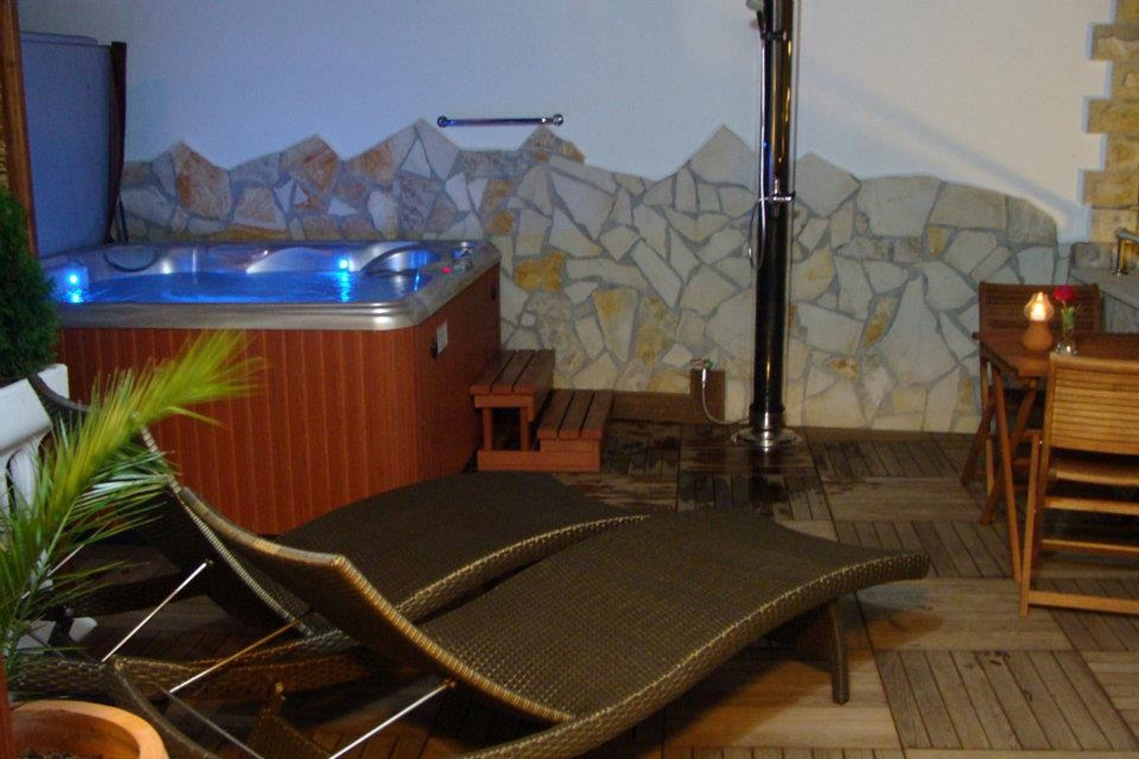 A hot tub with a stone wall backdrop, a lounge chair, and a small table with a candle.