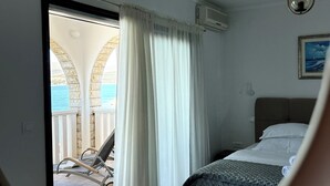 Een slaapkamer met een bed, een raam met gordijnen, een plafondventilator en uitzicht op het balkon.