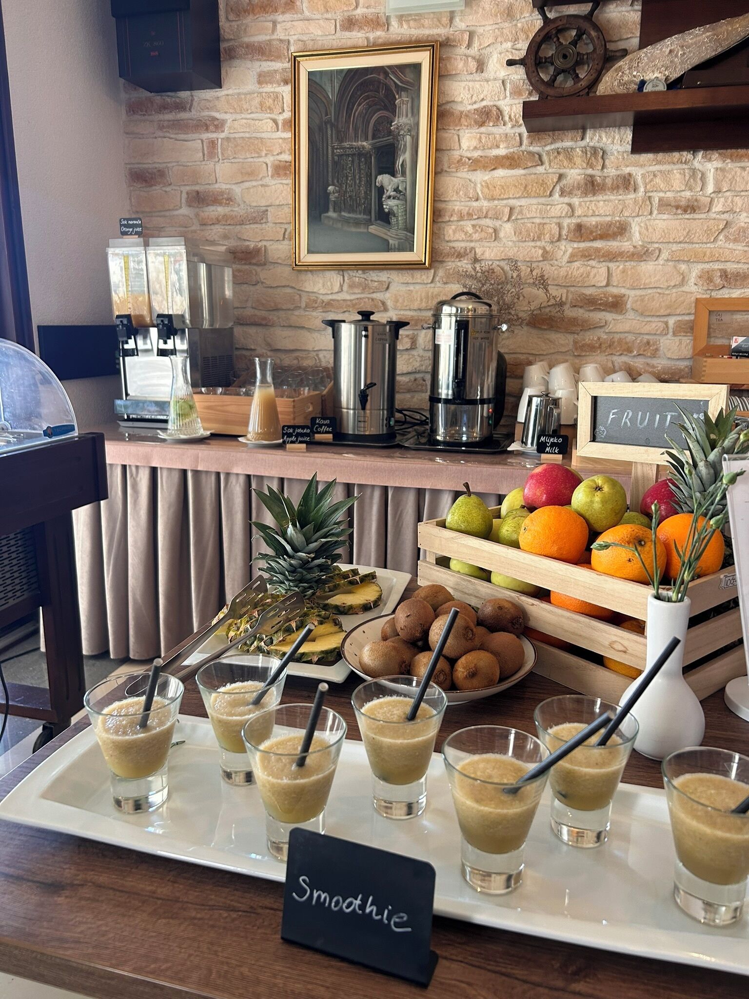 Ein Frühstücksbuffet mit Kaffeeautomaten, einer Obstauslage und einem Schild für Smoothies.