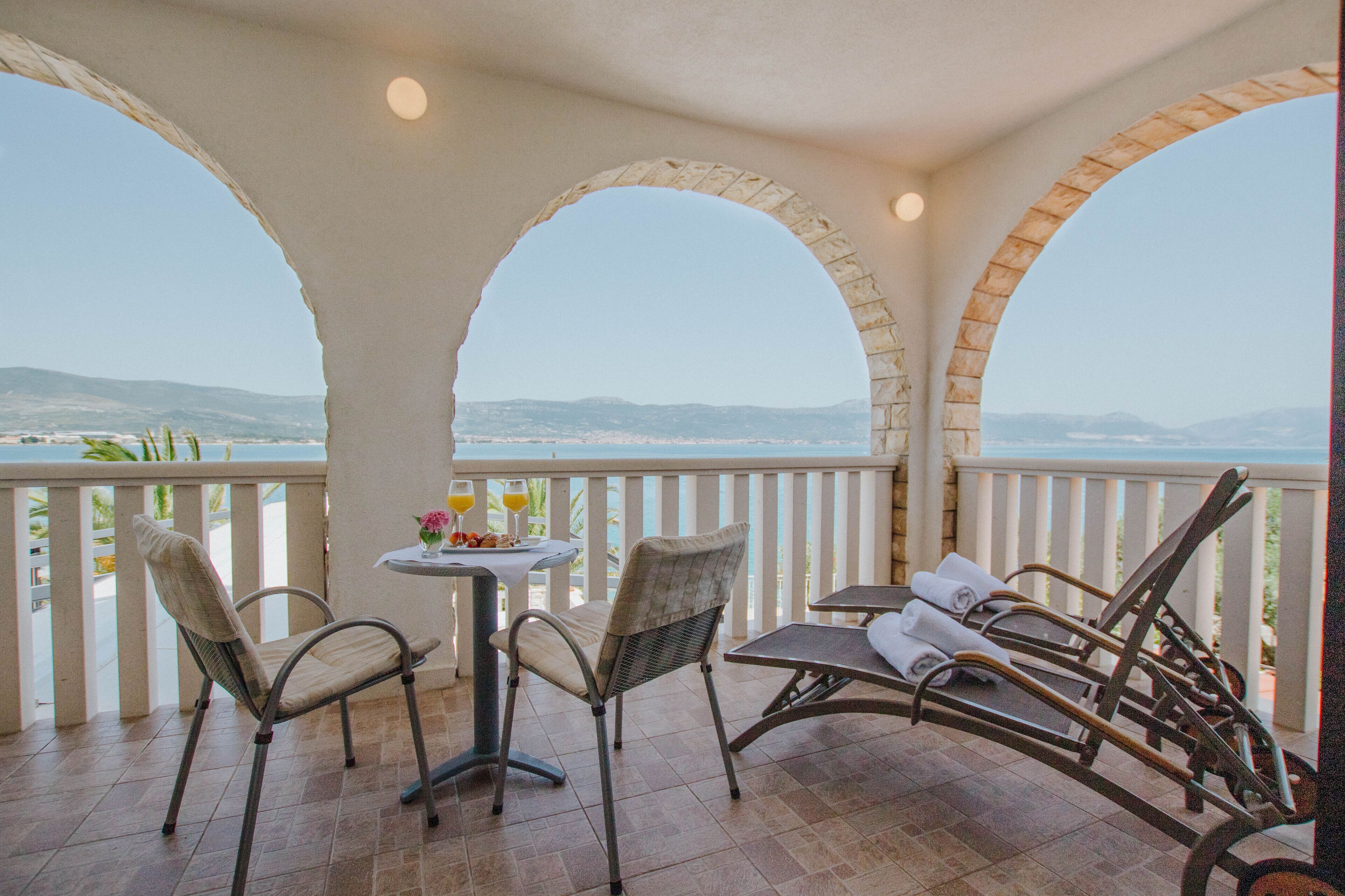 A balcony with two wicker chairs, a table with a glass of orange juice, and a view of the landscape.