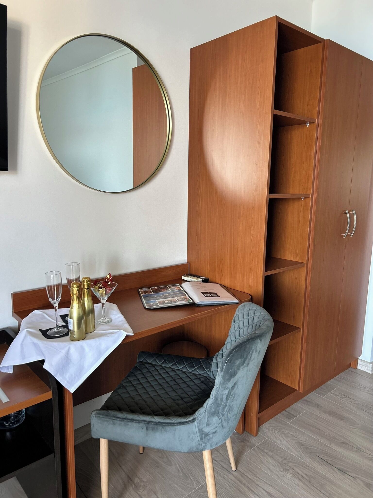 A compact room with a wooden desk, a chair, a wardrobe, and a round mirror on the wall.