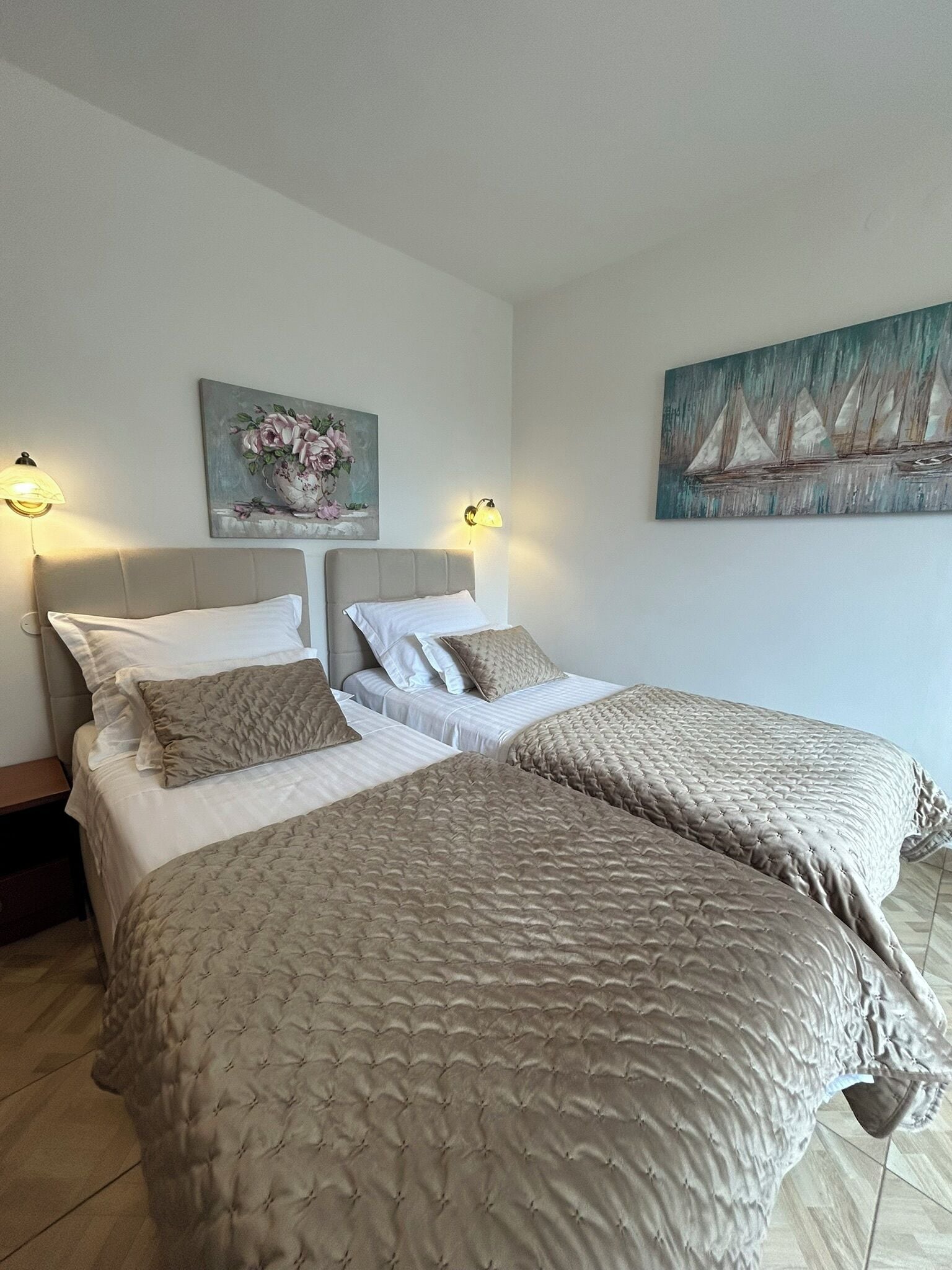 Une chambre d’hôtel avec deux lits, un tableau de fleurs et un tableau représentant des voiliers accroché au mur.