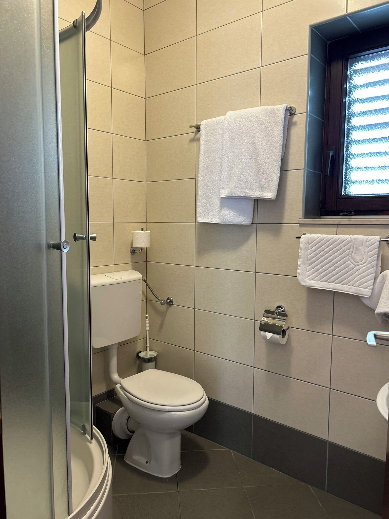 A bathroom with a toilet, a glass shower enclosure, and a window with blinds.