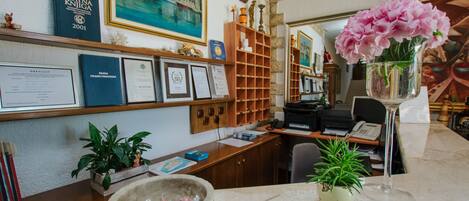 Un bureau bien aménagé, avec un bureau, des étagères où sont exposés des certificats, une horloge et un vase rempli de fleurs.