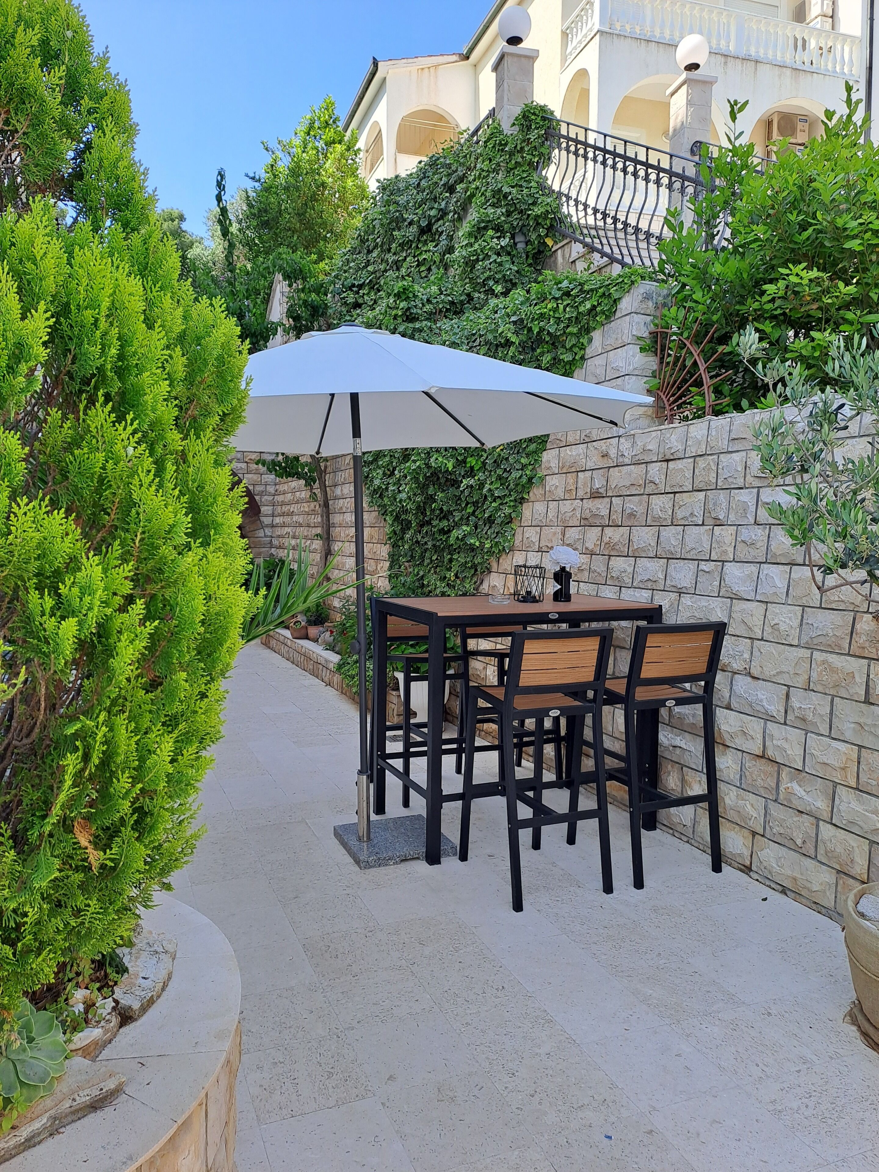 An outdoor patio with a table and chairs, a stone wall, and greenery.