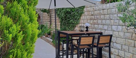 An outdoor patio with a table and chairs, a stone wall, and greenery.