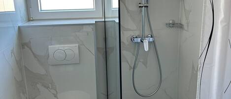 A modern bathroom with a glass-enclosed shower, a toilet, and a window above the sink.