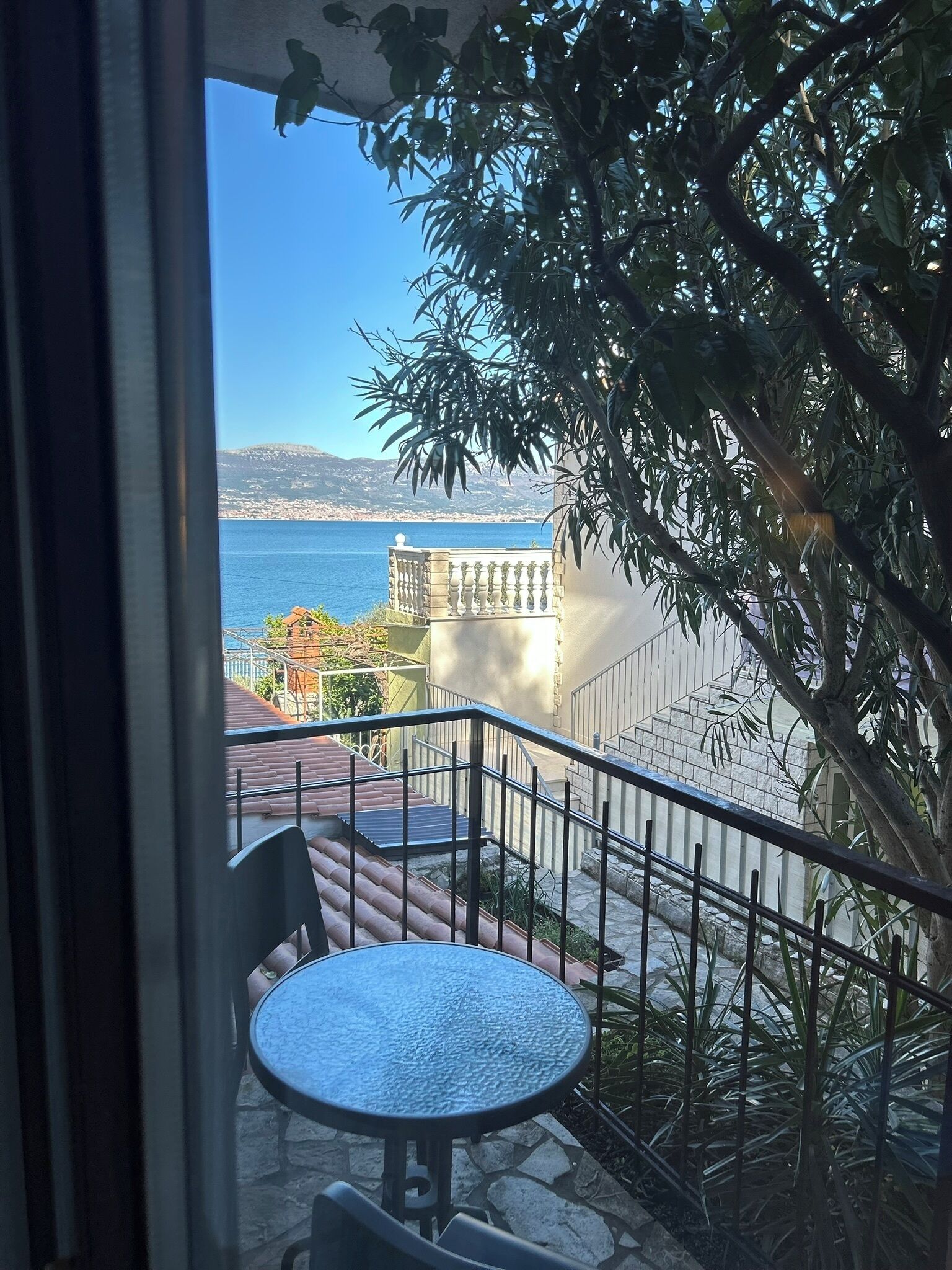 A balcony with a table and chairs, overlooking a body of water and a distant cityscape.