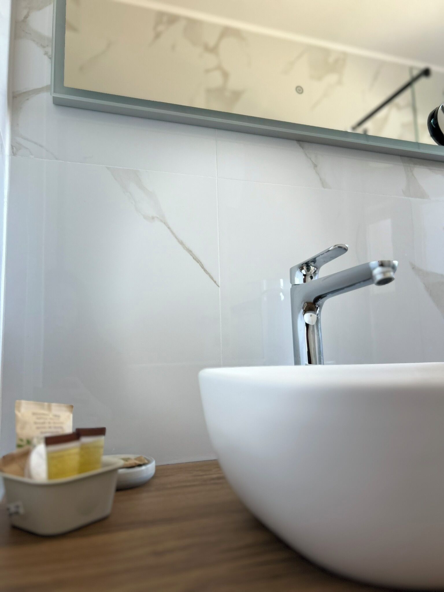 A bathroom with a white sink, a mirror above it, and a marble-tiled wall.