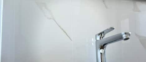 A bathroom with a white sink, a mirror above it, and a marble-tiled wall.
