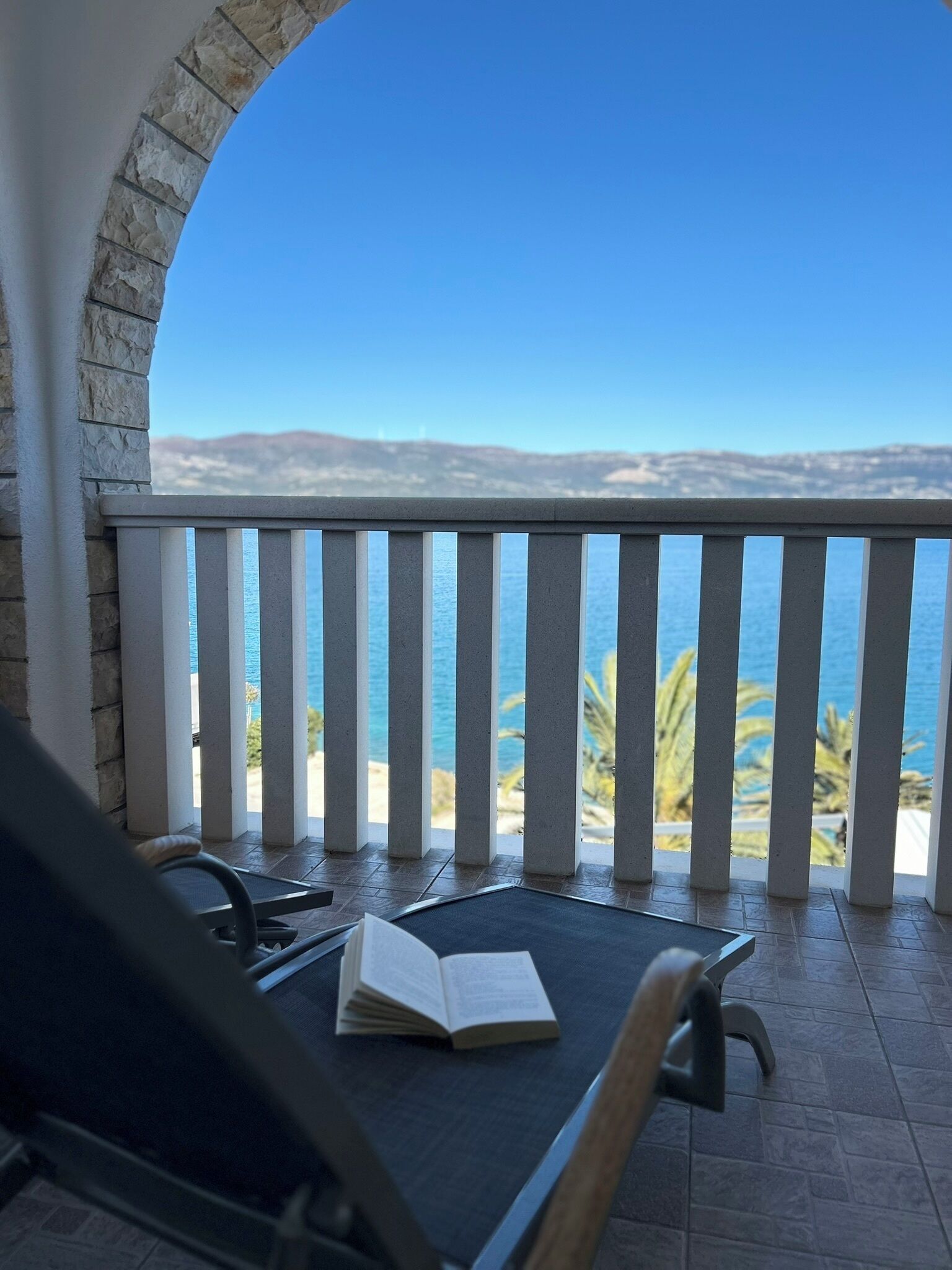 A balcony with a view of the sea, a book, and a chair.