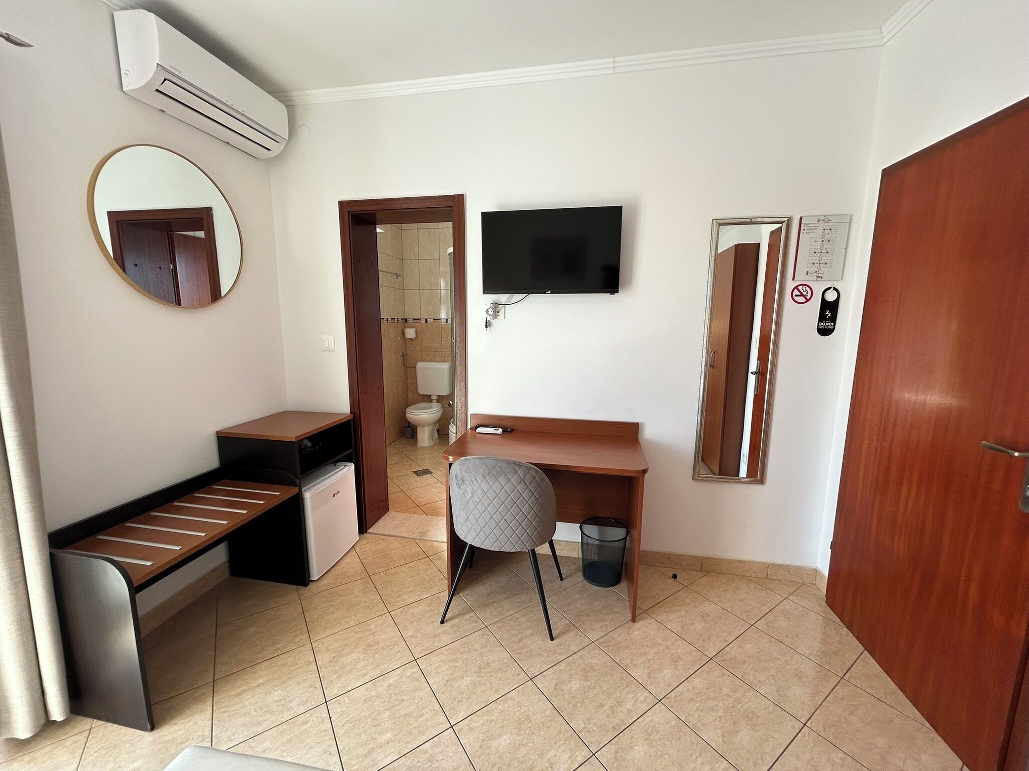Ein kleines Hotelzimmer mit Schreibtisch, Stuhl und einer Kochnische.