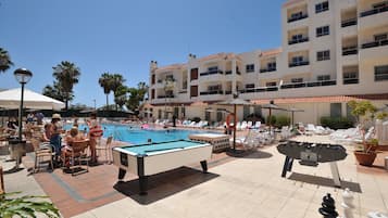 Un área de piscina con sillones de descanso, mesa de billar y mesa de fútbol de mesa.