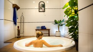 A person relaxing in a circular hot tub with a potted plant and a small table with towels. - Apartamentos Oro Blanco (Arona)