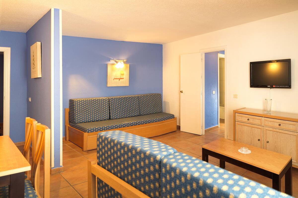 Una habitación con pared azul, un sofá, un televisor, un armario de madera y una zona de comedor.