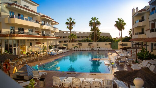 A hotel pool area with multiple lounge chairs, a swimming pool, and palm trees. - Apartamentos Oro Blanco (Arona)
