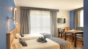 A hotel room with two beds, a desk, a chair, a television, and a window with curtains. - Apartamentos Oro Blanco (Arona)