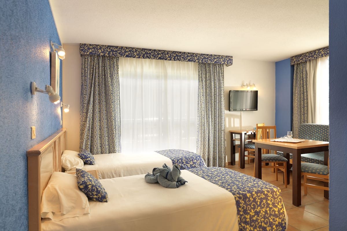 Habitación de hotel con dos camas, un escritorio, una silla, un televisor y una ventana con cortinas.