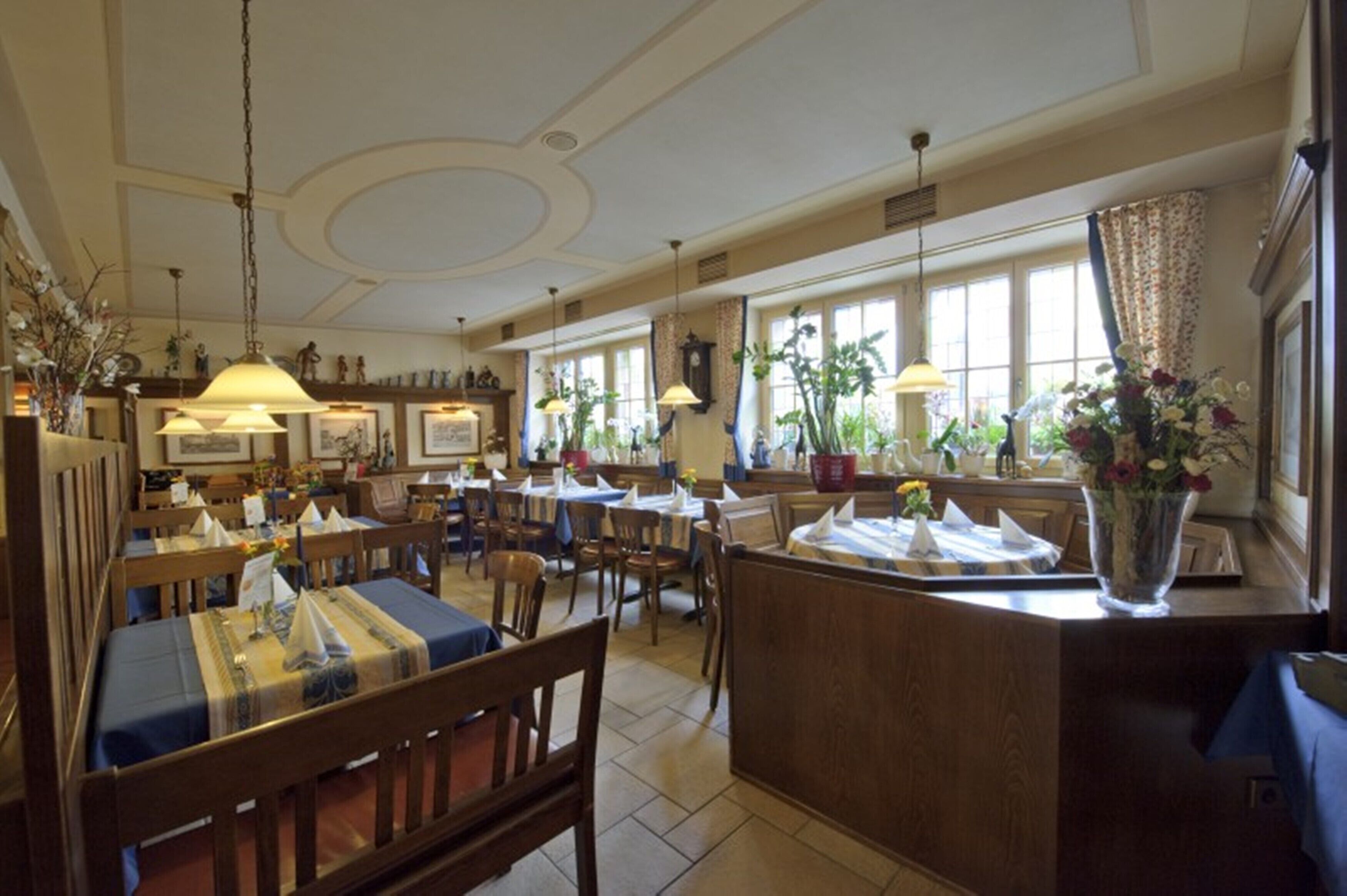 Un restaurant amb taules i cadires de fusta, una illa central amb mostrador, i grans finestres que deixen entrar llum natural.