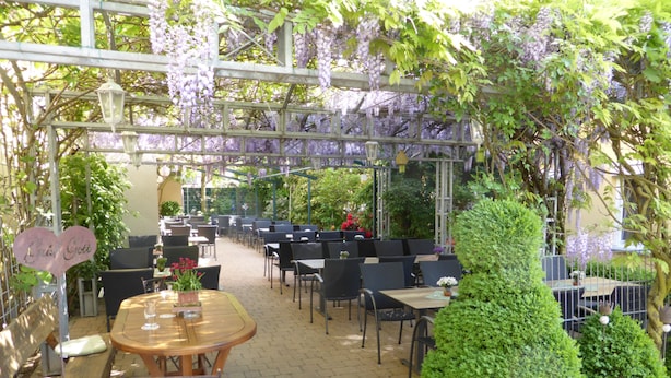 An outdoor cafe with tables and chairs, a pergola with hanging purple flowers, and a sign that reads "Café Gotti". - Hotel Adlerbräu (Gunzenhausen)