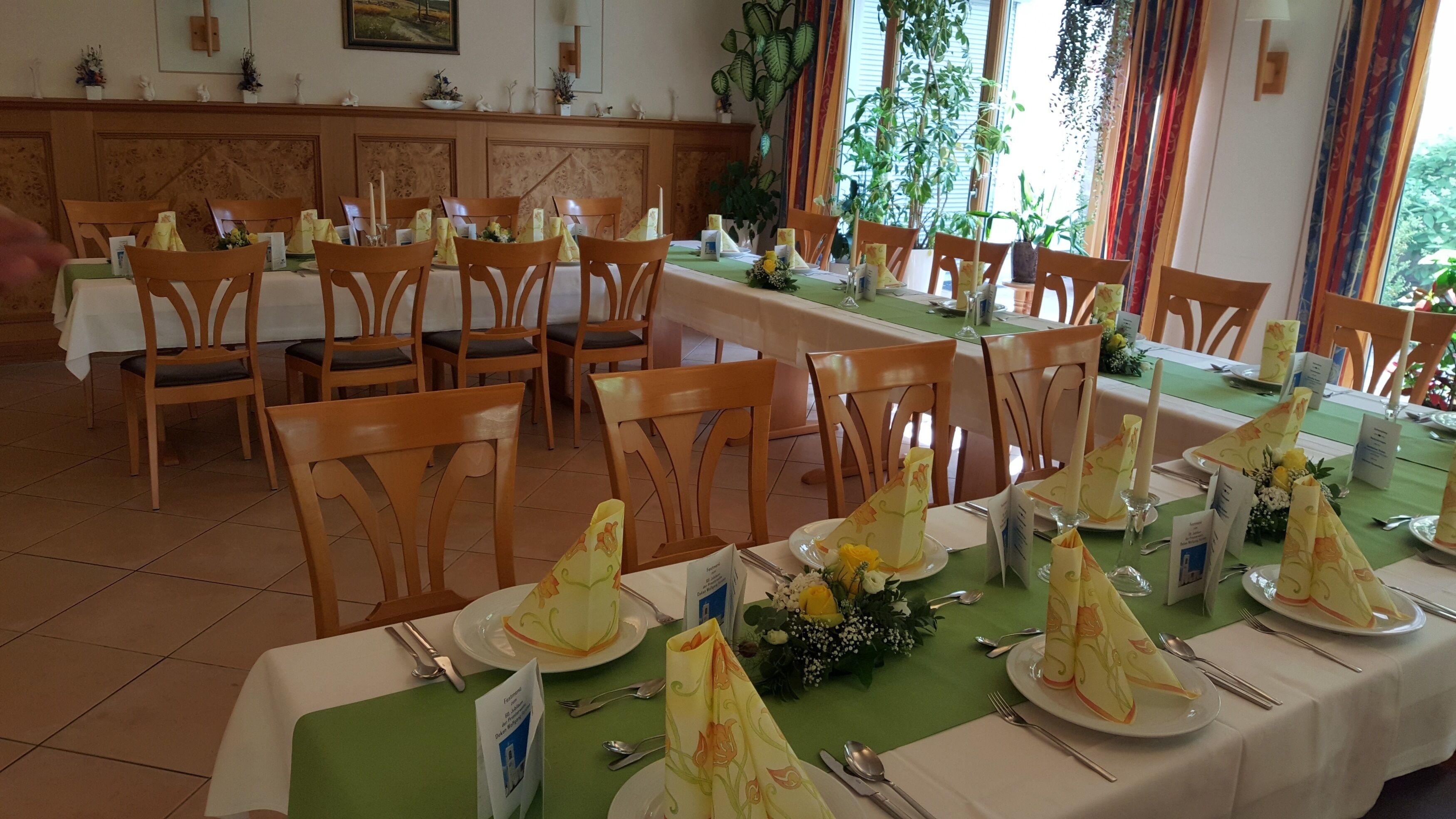 Un comedor con varias mesas dispuestas para el servicio, sillas de madera y un mantel verde.