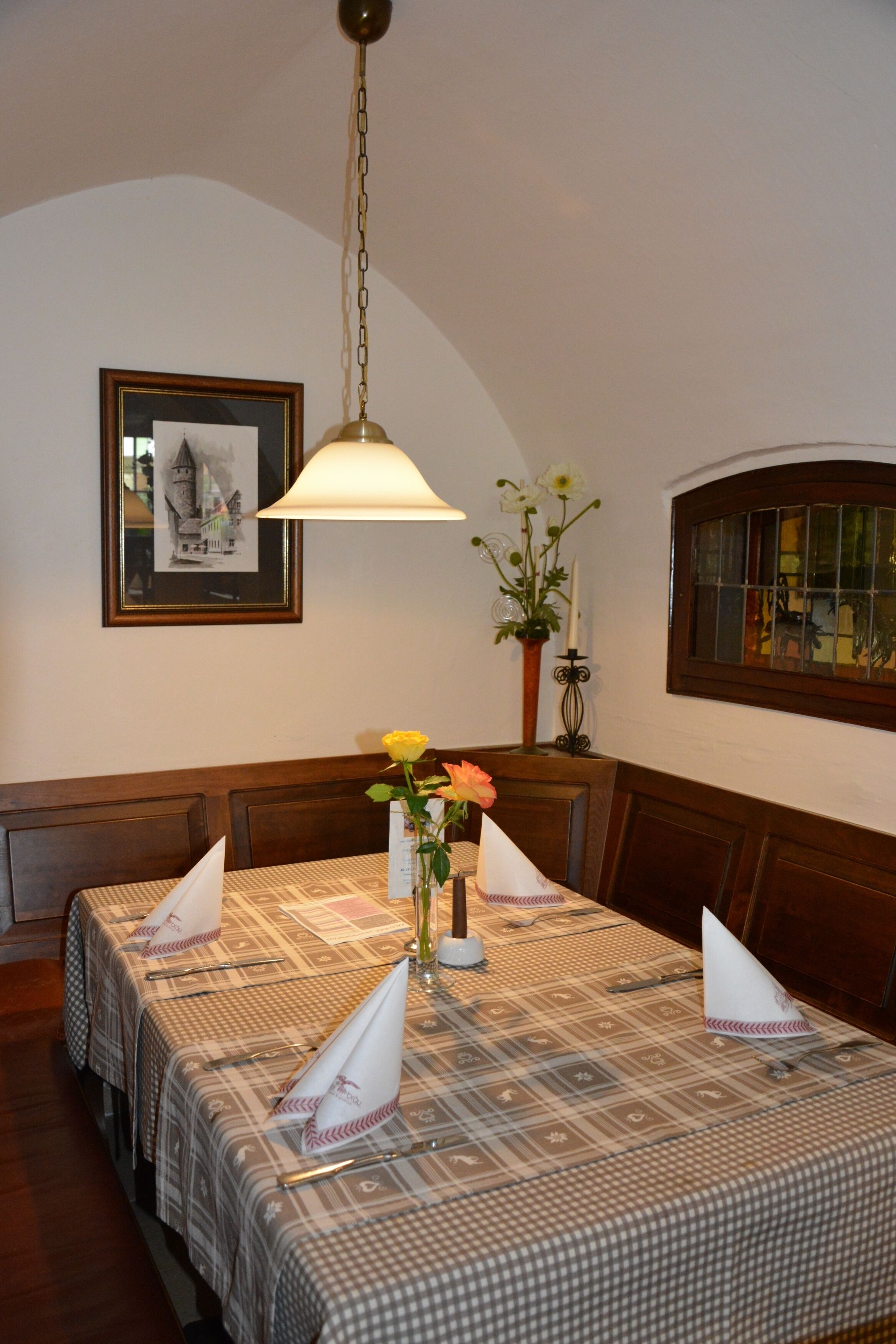 Un coin repas avec une nappe à carreaux, un vase rempli de fleurs et un tableau encadré accroché au mur.