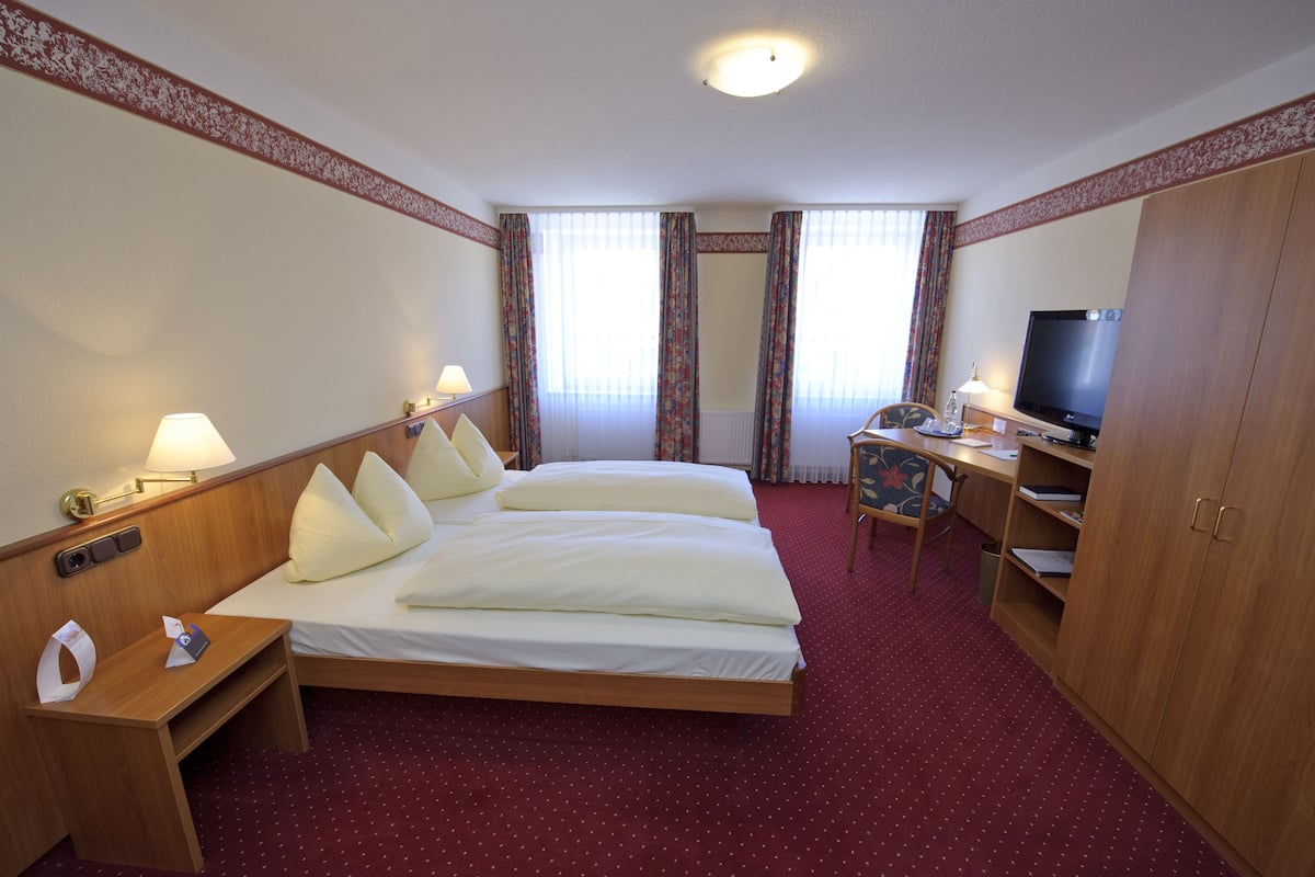 A hotel room with a double bed, a desk with a television, a chair, and a small table.