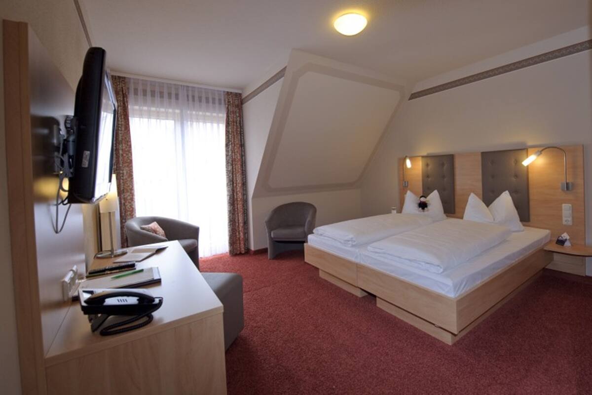 A hotel room with a bed, desk, chair, and a television.