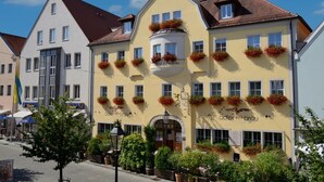 A yellow building with multiple windows and flower boxes on the facade, located on a cobblestone street. - Hotel Adlerbräu (Gunzenhausen)