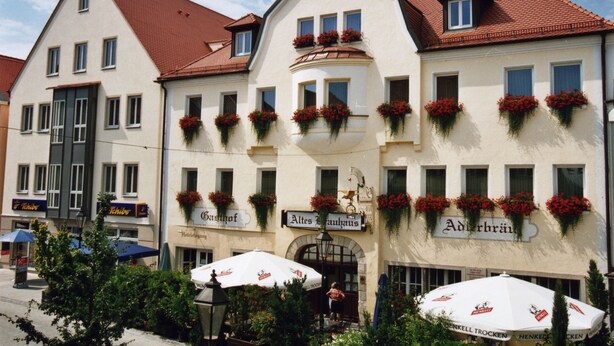 A traditional European hotel with multiple windows, flower boxes, and outdoor seating areas. - Hotel Adlerbräu (Gunzenhausen)